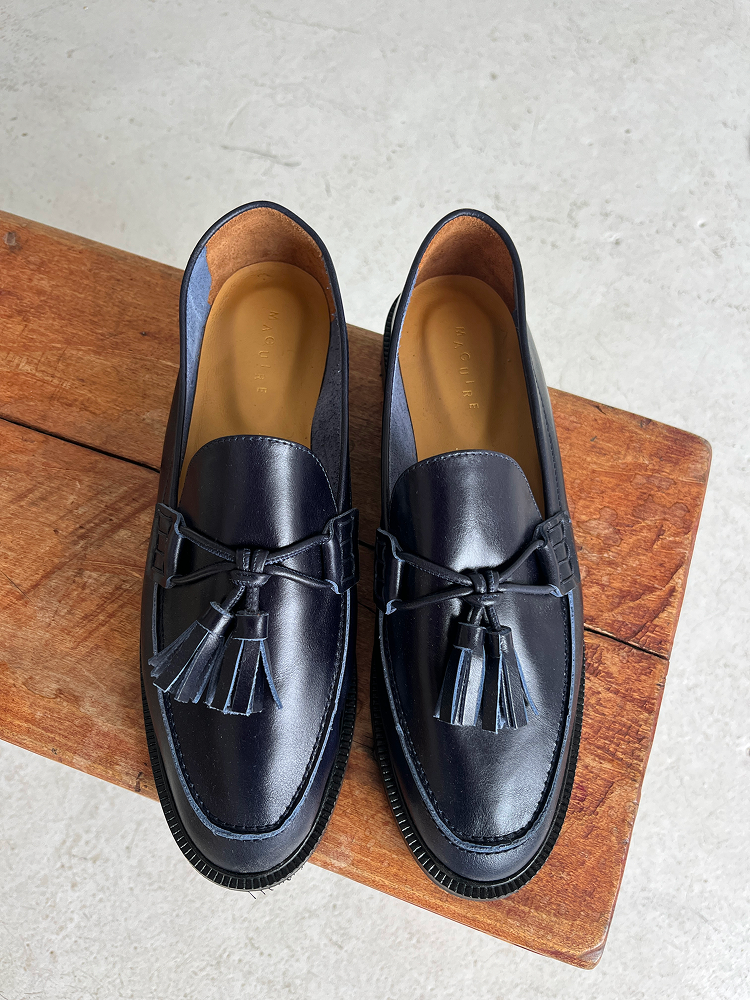 Pair of navy loafers with pompoms on wooden stool, white floor background