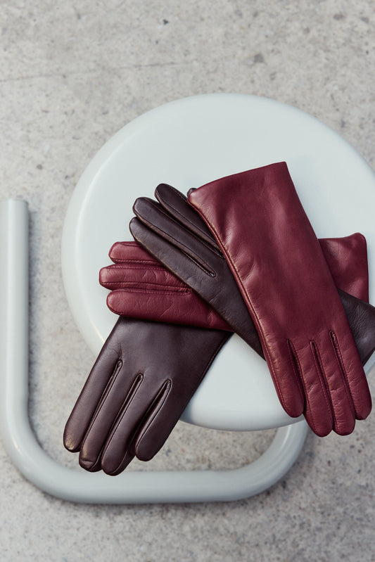 Pair of brown leather gloves on a white chair with a gray background