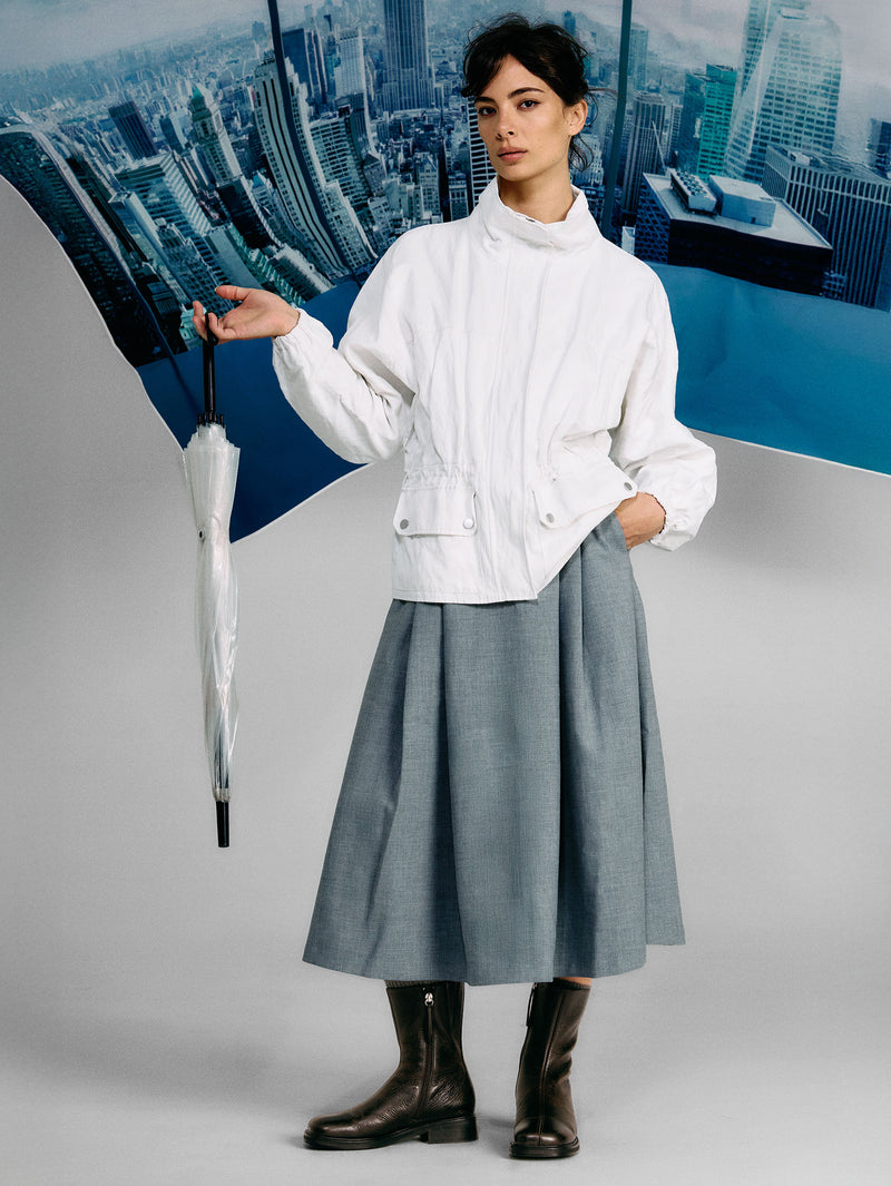 Person wearing a white jacket and gray skirt holding an umbrella with a cityscape background