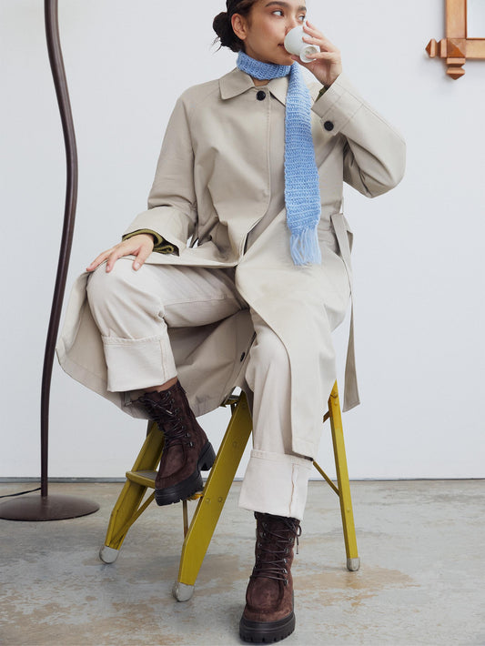 A brown suede chunky combat boot with lace-up closure and metal hardware worn with a nude outfit.