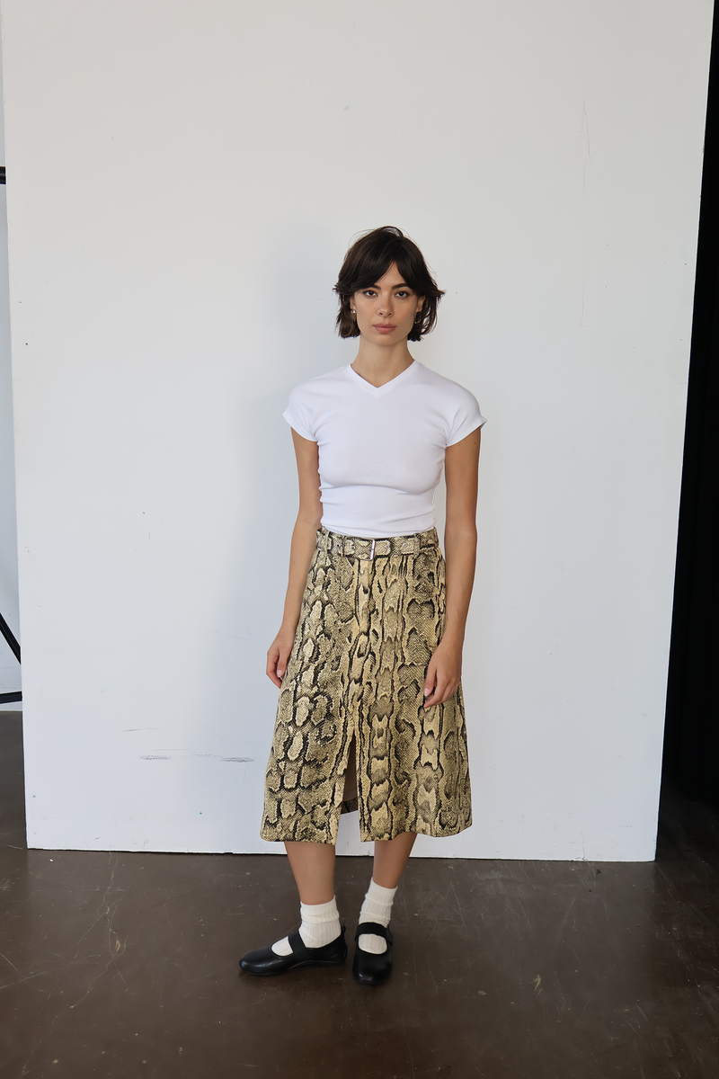 Person wearing a white t-shirt and snake print skirt against a plain background