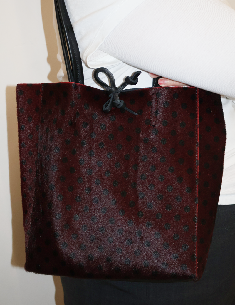 Carpi tote bag Bordeaux with black dot pattern held by a person wearing a white shirt.