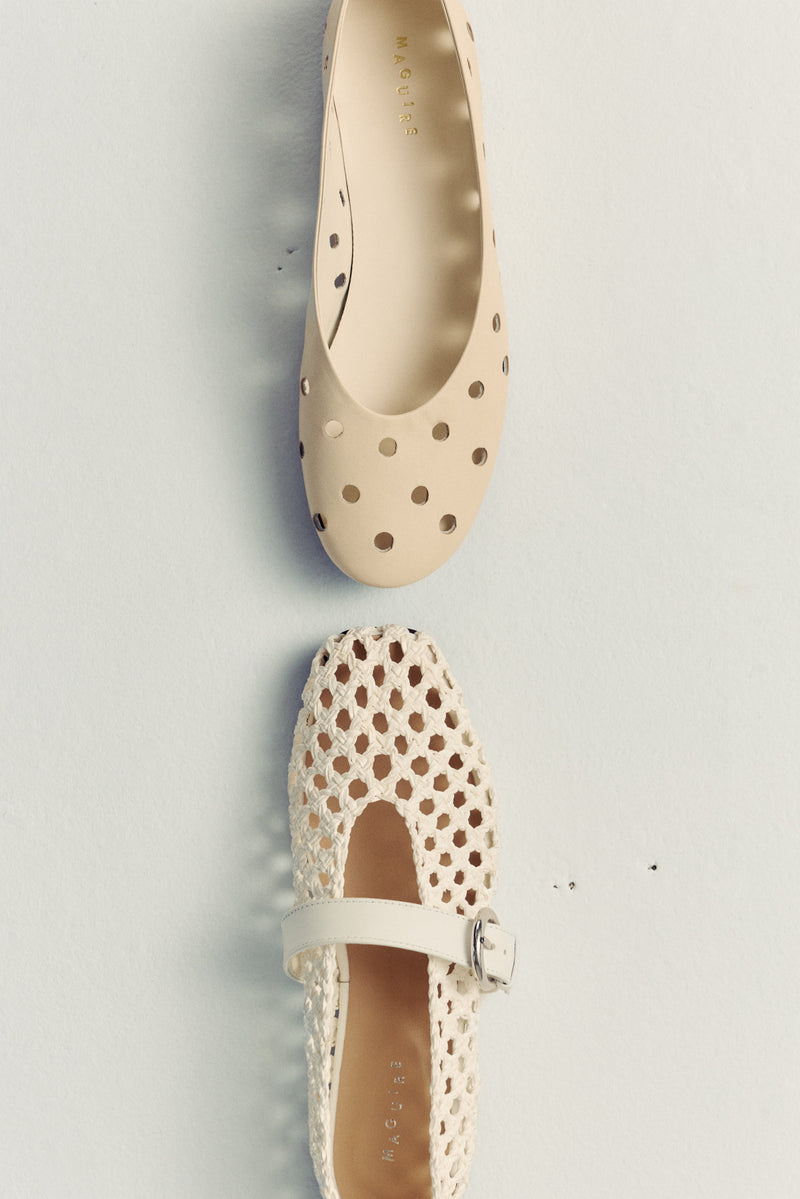 two ballet flats on white floor facing each oter. both leather and cream coloured with perforated details