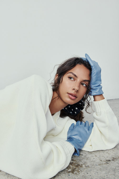 Person wearing a white sweater and Alpi blue gloves on a plain background