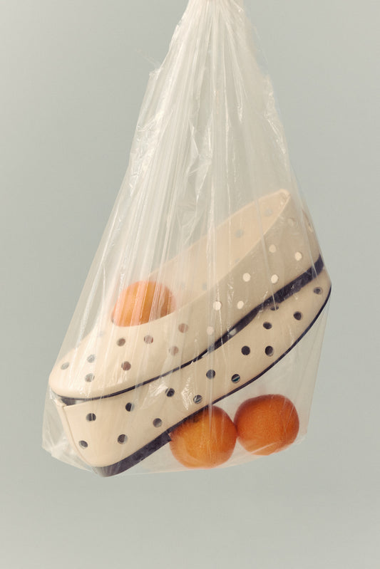 cream ballet flat with round cut outs in clear plastic blag with three clementines on white background