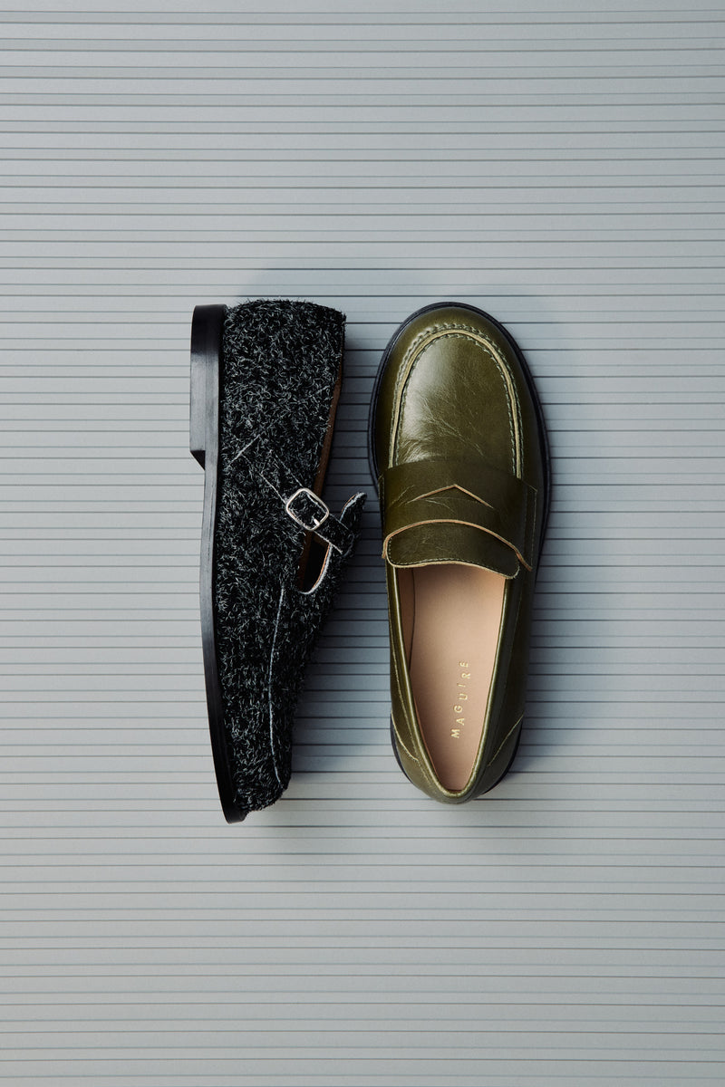 Two loafers, one black and one green, on a textured gray surface.