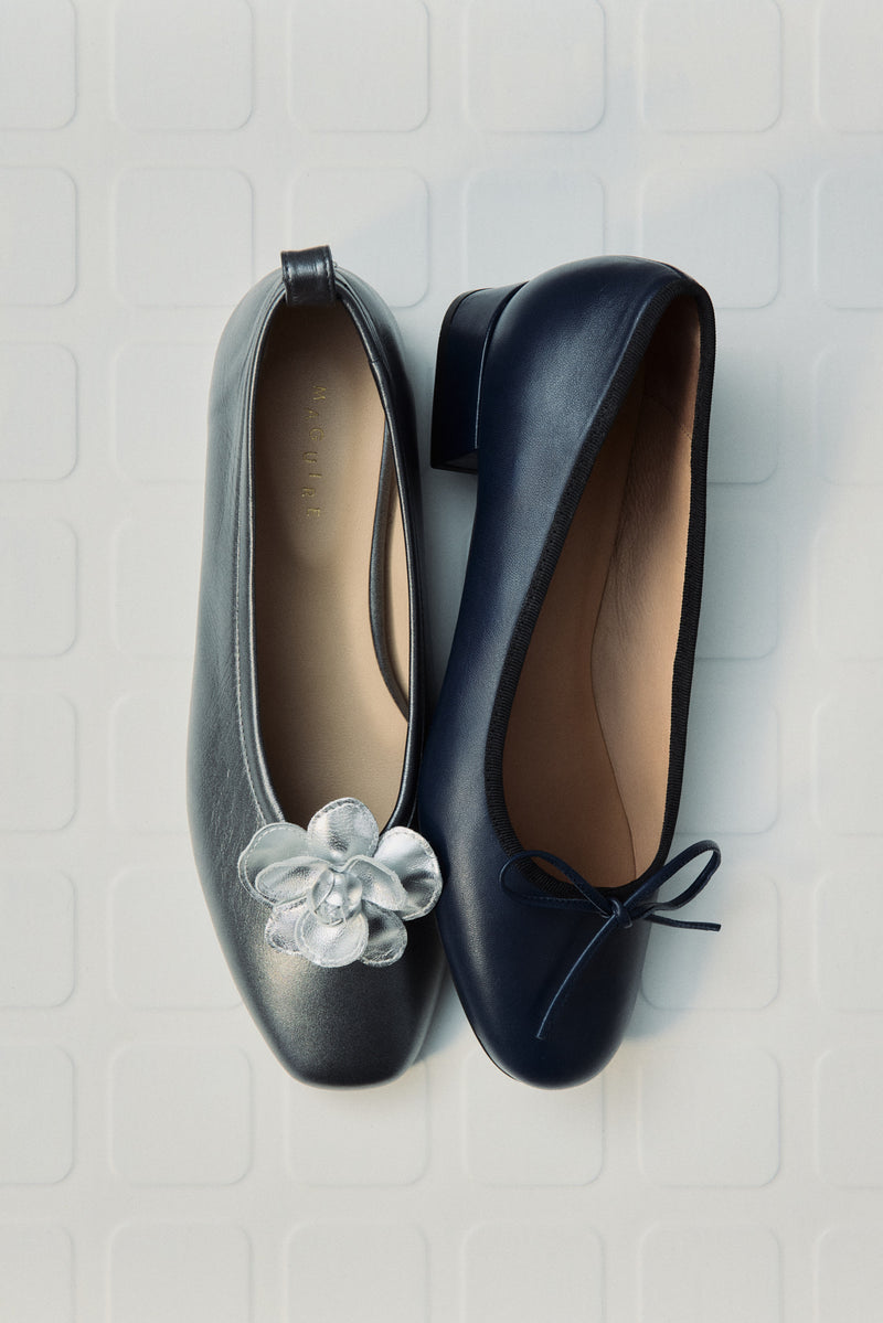 Pair of black shoes with a decorative flower on a textured silver surface