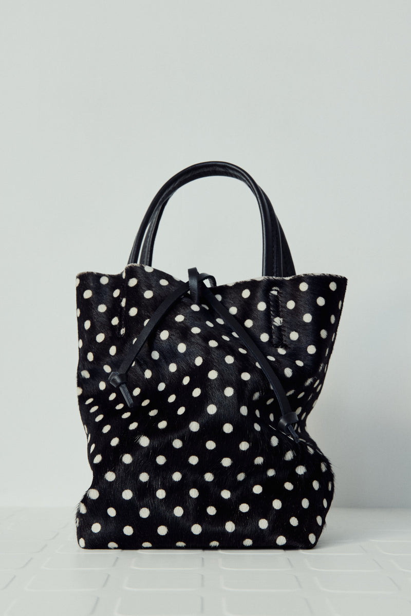Black tote bag with white polka dots on a light gray background