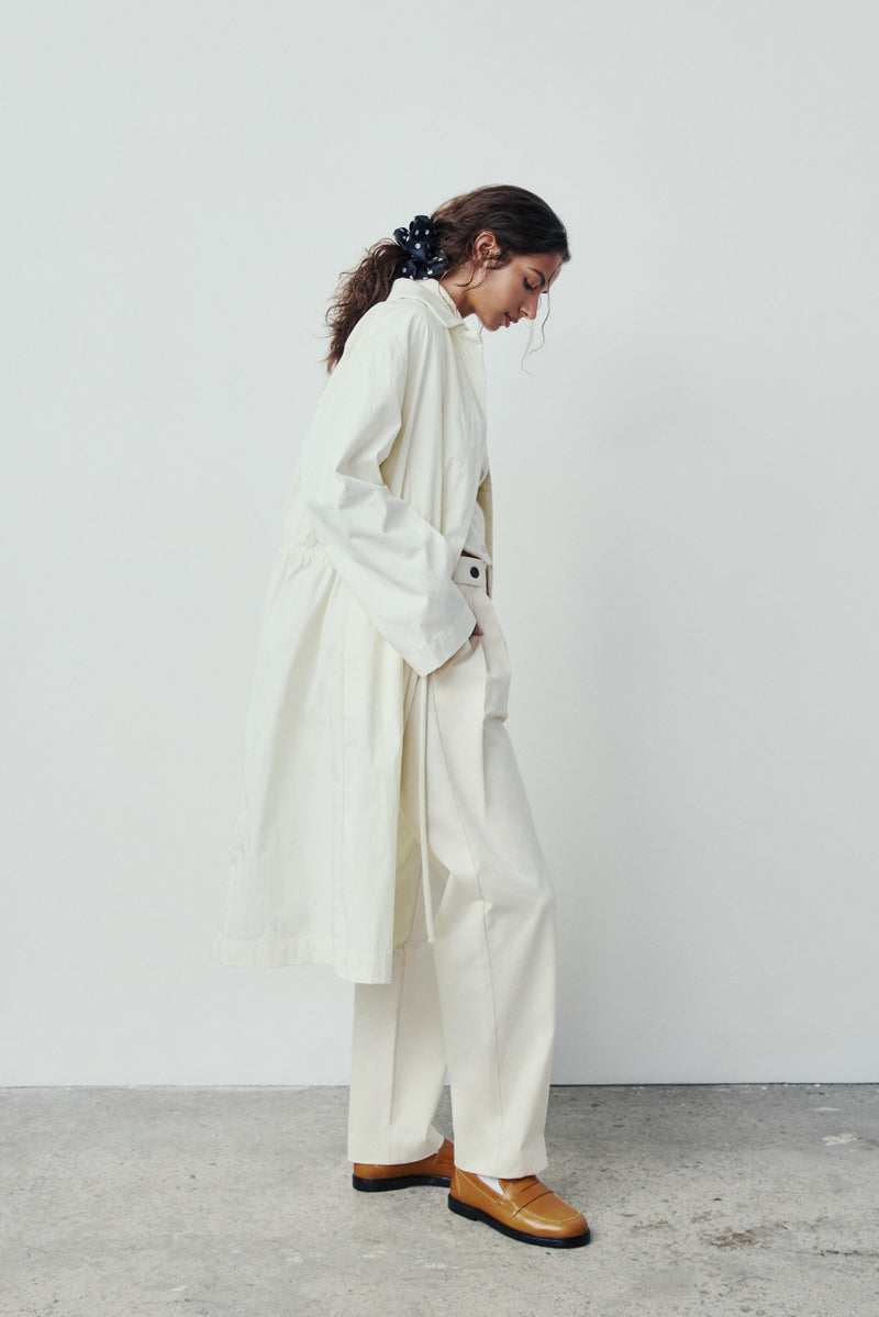 Person wearing a white coat and pants with tan shoes against a plain background