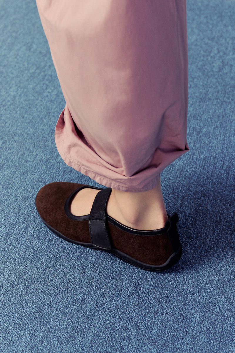 bottom half of a half, woman wearing dusty pink pants with brown flats on blue carpet.