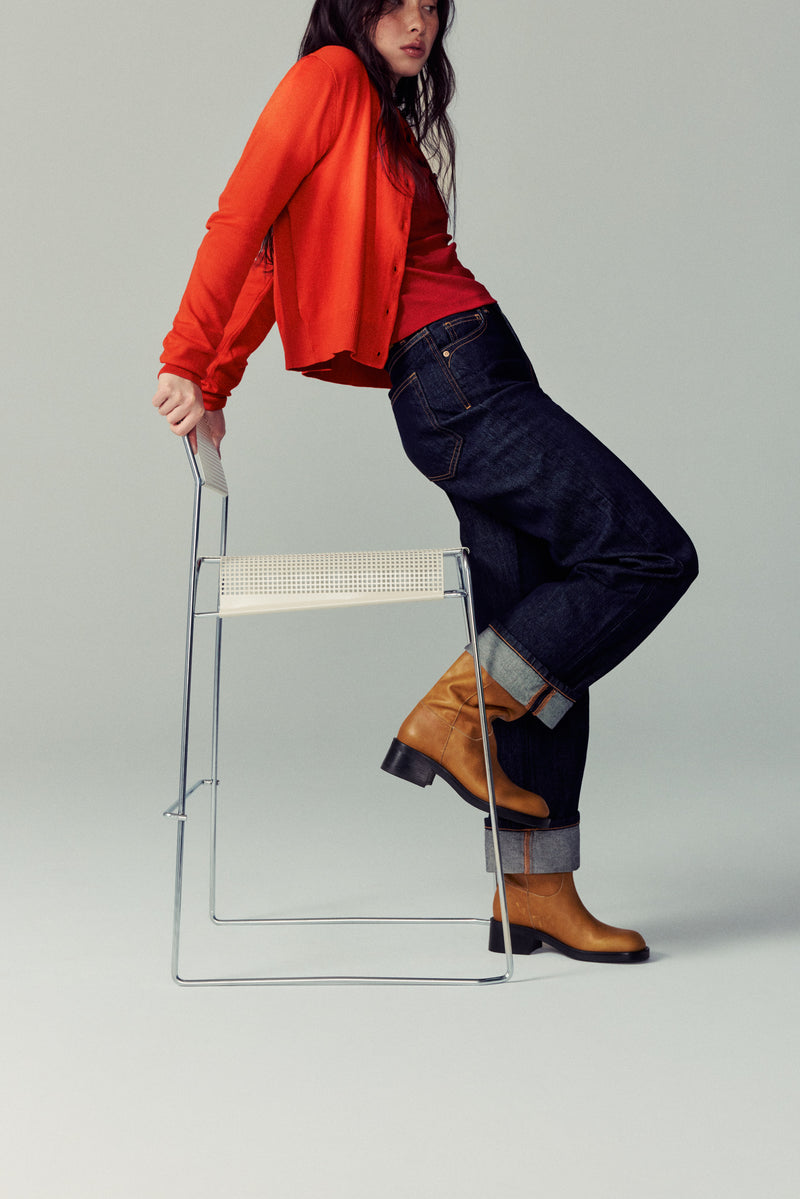 Person wearing a red shirt and blue jeans standing on a clear stool against a gray background with Lucca Boots in Dijon.