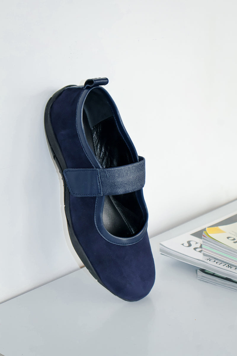 navy ballet flat leaning against wall, books pictured in the background