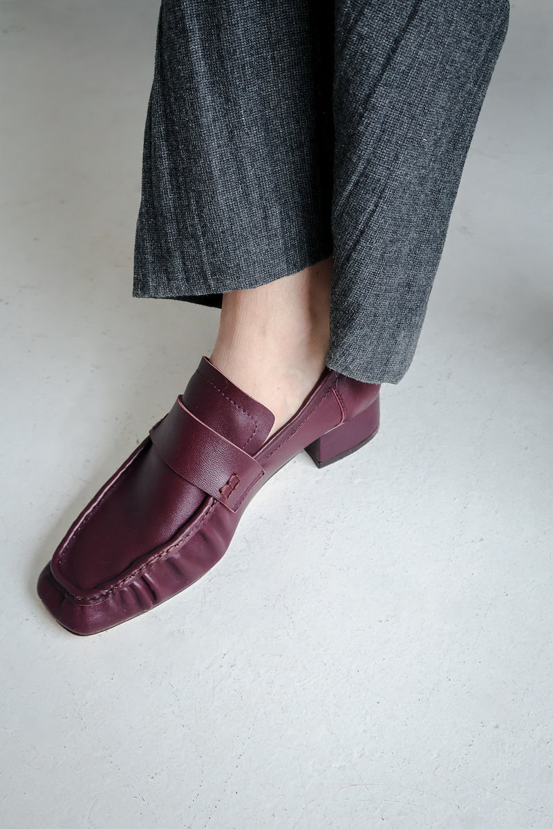 Bordeaux loafers worn with gray pants on a light background