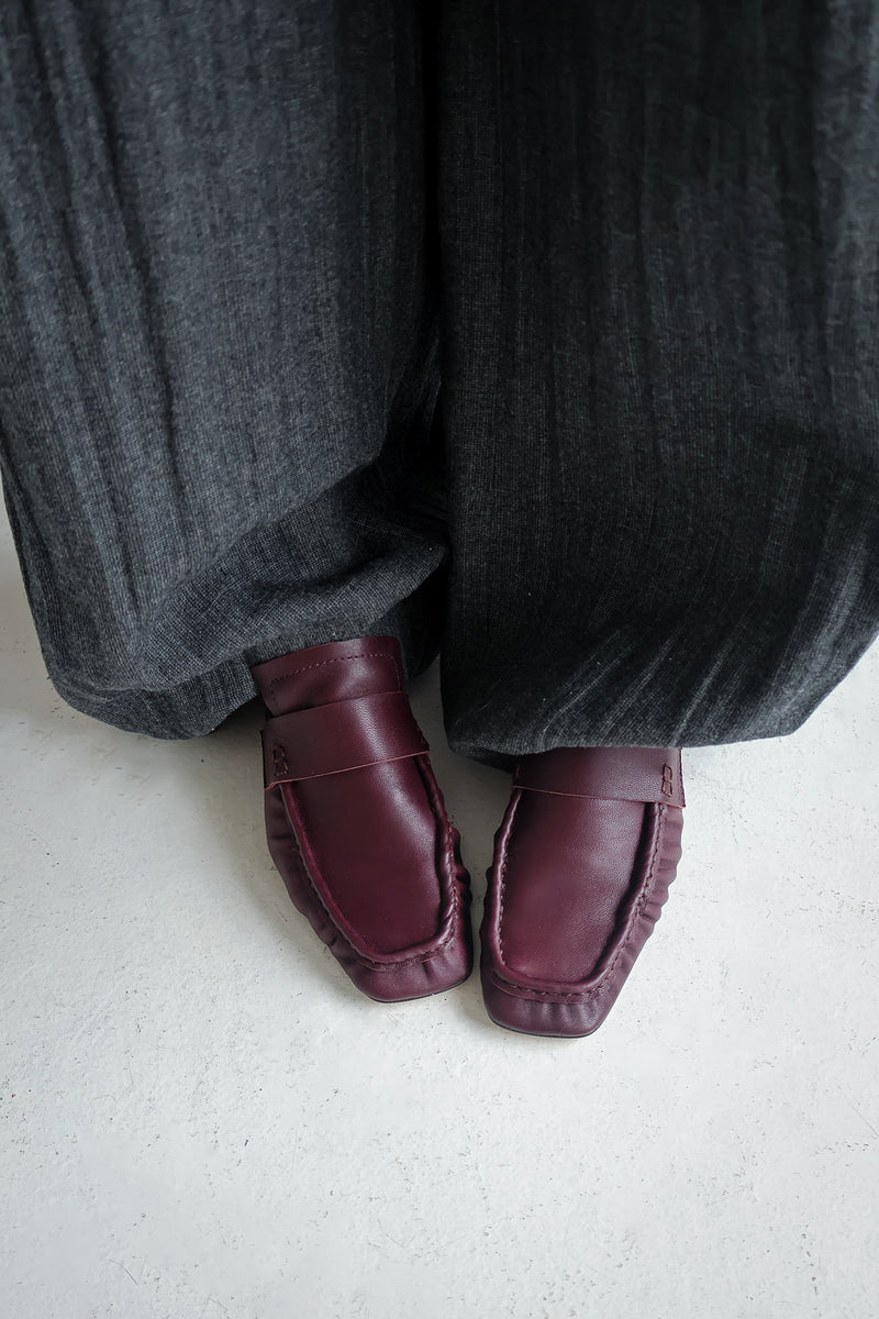 Bordeaux loafers worn with gray pants on a light background