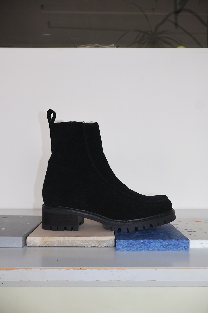 Shearling lined winter boot with a front piping detail, in a black suede with a black lug outsole. 