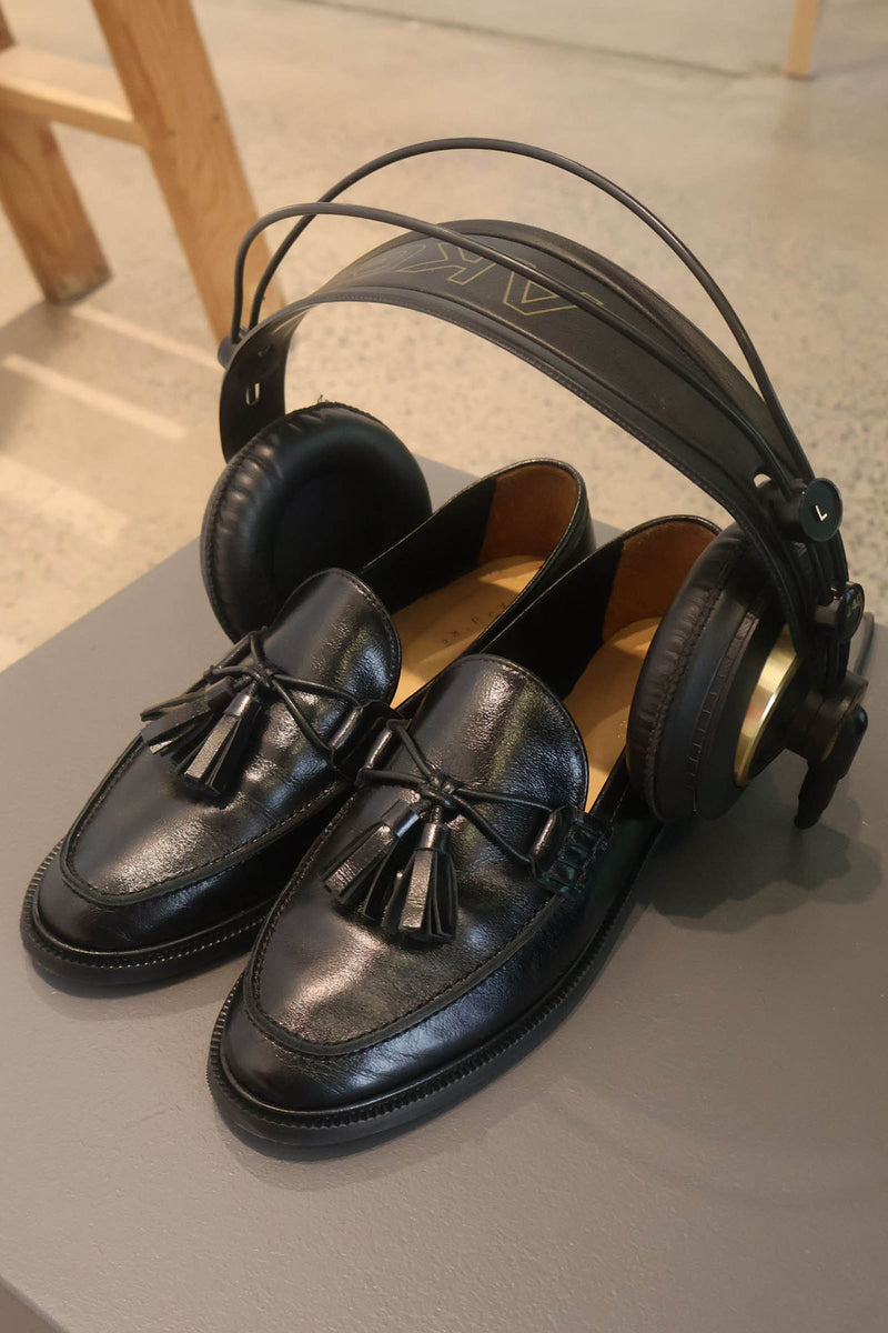 Black loafers with tassels and a pair of black headphones on a gray surface.