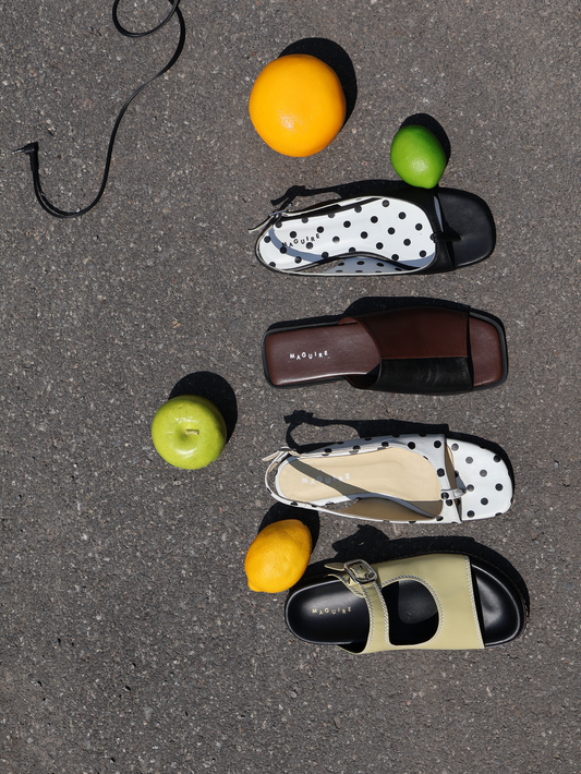 Four pairs of shoes on a gray surface with fruits around them