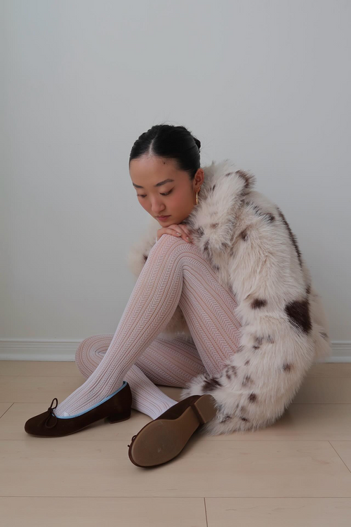 Woman sitting on the floor wearing a white fur coat and pink tights with Covelo Brown.