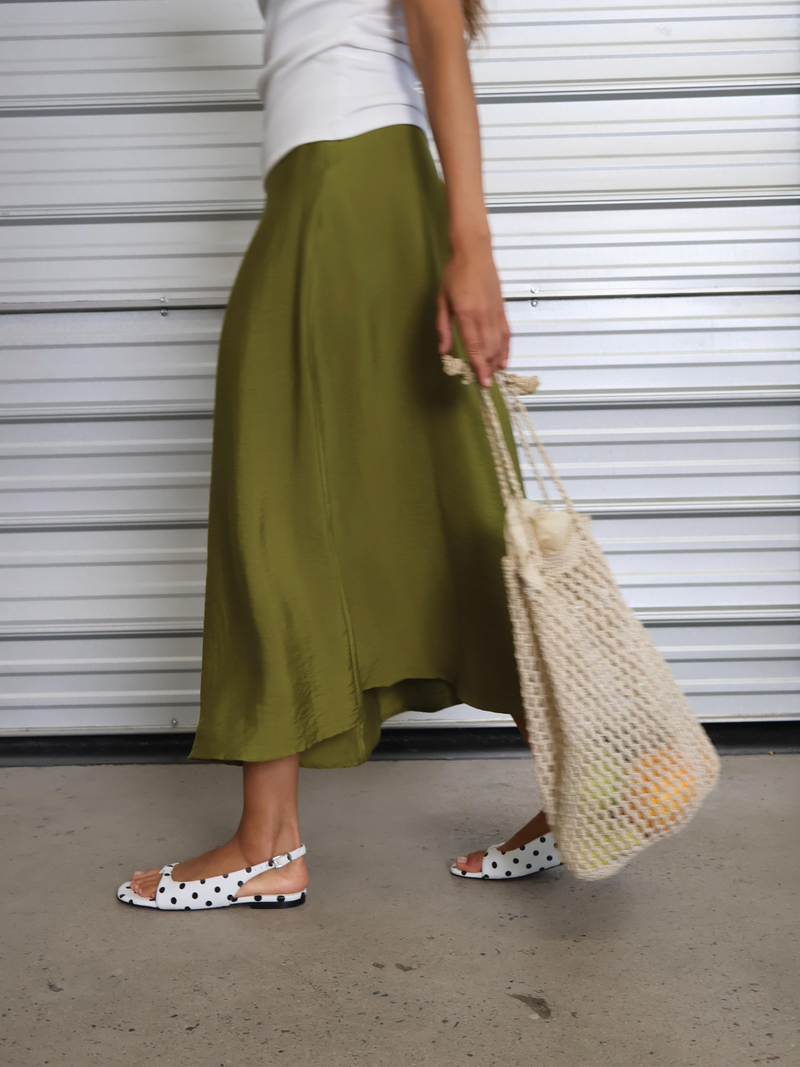Woman with a green skirt wearing black and white polka dot sandal and earring a beige bag.