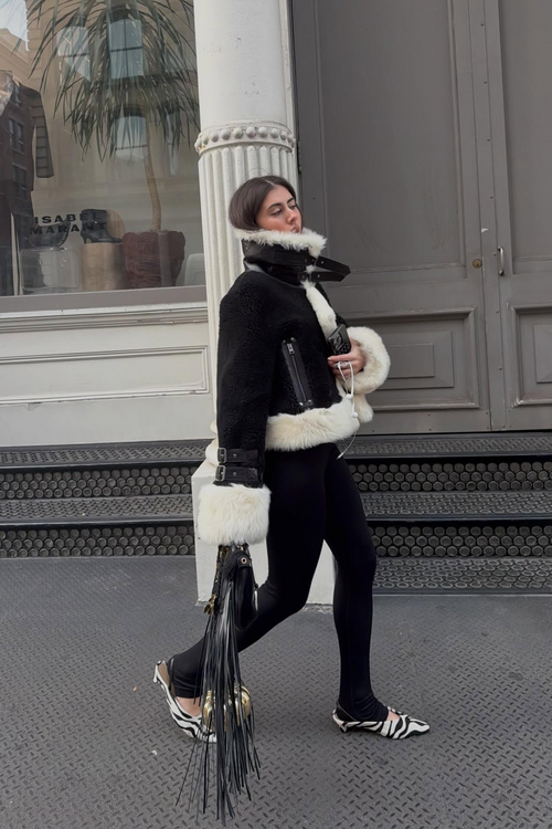 Person wearing a stylish outfit with a black jacket and white fur trim, standing on a street with Floresta Zebra mules.