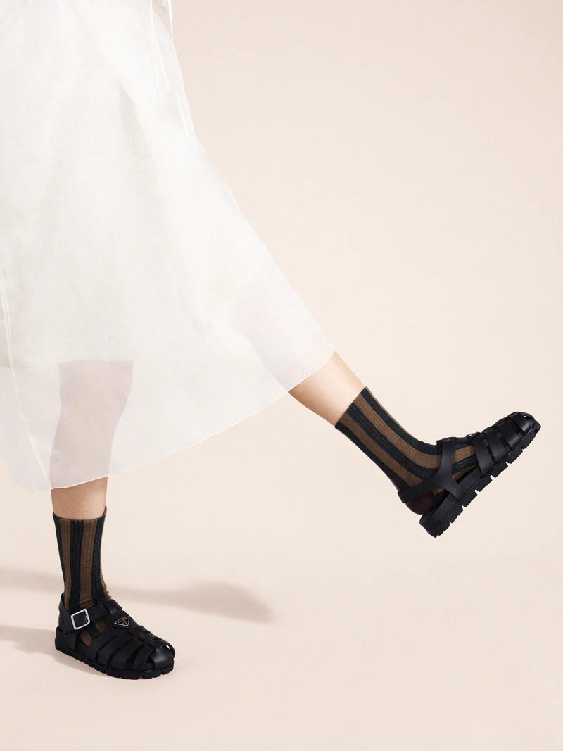 Person wearing black sandals and sheer black socks on a beige background