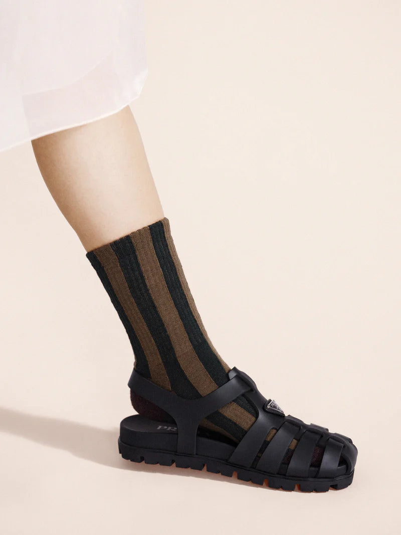 Black sandal worn with a striped sock on a beige background
