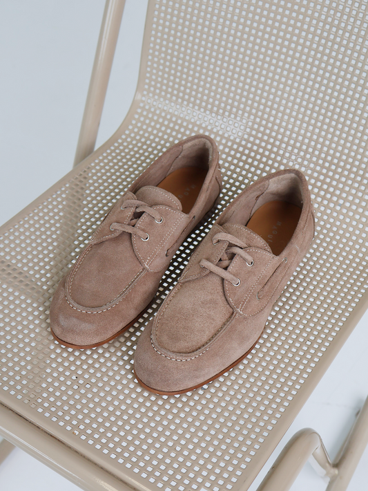 Pair of beige suede shoes on a beige chair with a white background